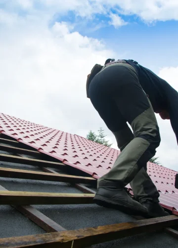 Construction workers installing a new red metal roof on a building.