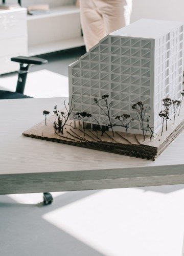 An architectural scale model of a modern building with miniature trees on a desk.