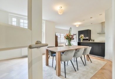 Modern open-concept dining area and kitchen with a wooden table, grey chairs, and hardwood floors