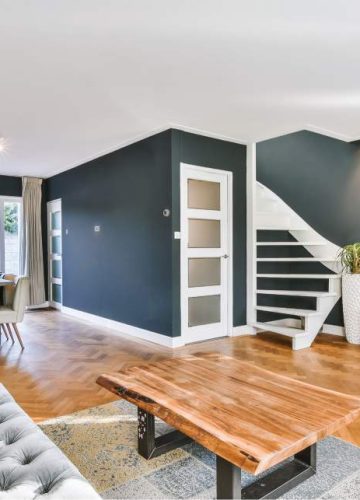 Modern open-concept living room and dining area with wood floors, a grey sofa, and dark blue accent walls.
